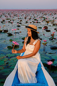 海莉摄影照片_泰国乌隆他尼的红莲海 Kumphawapi 满是粉红色的花朵，泰国妇女在一艘船上。