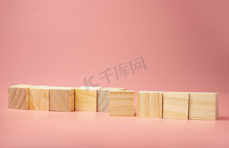 一个空的木制立方体排列在粉红色的背景上。