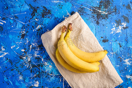 蓝色创意纹理摄影照片_蓝色带纹理背景上带桌布的香蕉果实