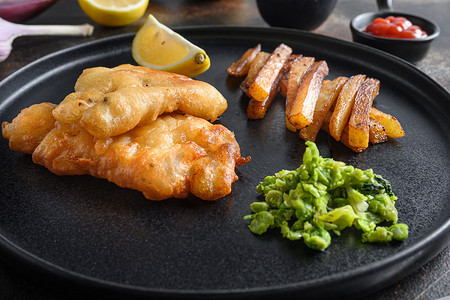 英国传统炸鱼薯条，配以捣碎的薄荷豌豆、塔塔酱垂直侧视图，在黑盘上特写细节侧视图。