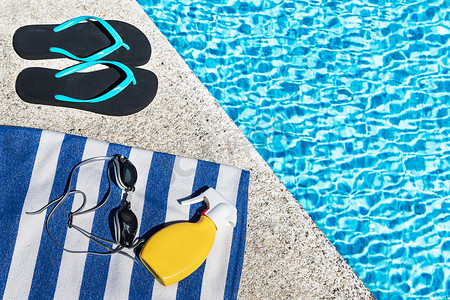 人字拖，防晒喷雾喷在泳池边的蓝白条纹毛巾上。