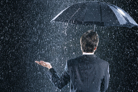 一位商人在倾盆大雨中在雨伞下保持干燥的后视图