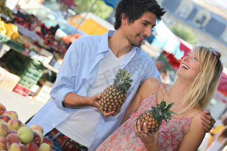 市场摊位摄影照片_在市场摊位上拿着菠萝的年轻夫妇