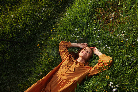 一个快乐、轻松的女人，躺在绿草丛中休息，穿着橙色长裙，闭着眼睛，脸上带着愉快的微笑，享受与自然的和谐和休养