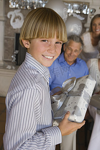 十几岁男孩拿着礼物给他祖父的肖像，背景是家人