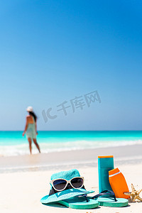 白色沙滩背景海洋上的防晒霜瓶、太阳镜、人字拖
