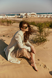 坐在海边摄影照片_一位美丽时尚女性坐在海边沙滩上放松的肖像