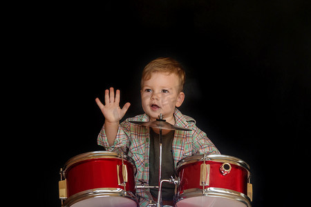 架子鼓通鼓摄影照片_两岁的白人男孩正在演奏在黑色背景下被隔离的架子鼓