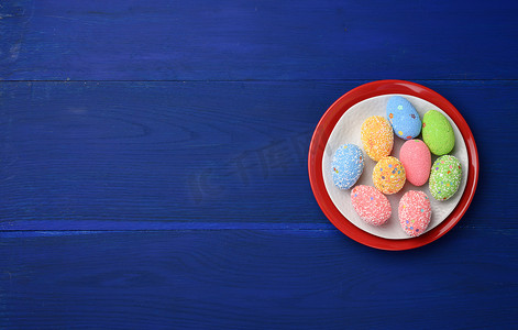 蓝色木板背景上圆形白色陶瓷盘中的装饰性复活节彩蛋
