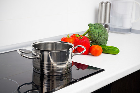 白色的现代厨房摄影照片_带感应炉的现代厨房中的锅和蔬菜