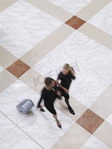 两个模糊的女商人带着手提箱在瓷砖地板上行走的高视图