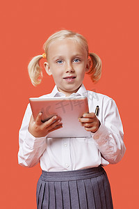 橙色背景中拿着平板电脑的快乐年轻女学生的肖像