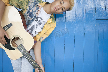 一个十几岁男孩在木镶板墙上弹吉他的肖像