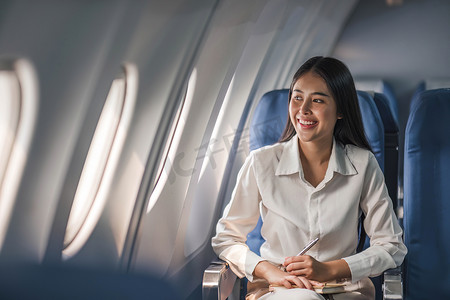年轻漂亮的女孩坐在包机或商务喷气式飞机的乘客座位上，靠近舷窗，微笑着
