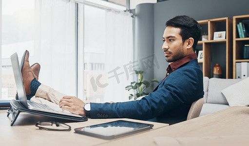 放松商人，双脚放在办公桌上，在笔记本电脑上工作，以获得工作信心、生产力和成功的职业生涯。
