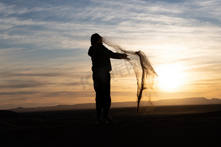 夕阳下在撒哈拉沙漠中跳跃和扔沙子的人的剪影