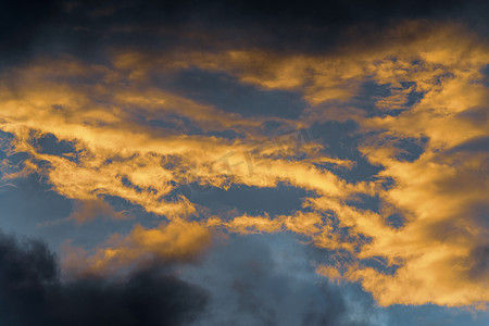 照亮黑暗摄影照片_日落时消失的光线照亮的金色蓬松云和漂浮在阳光明媚的蓝天上的黑暗雷云改变季节天气