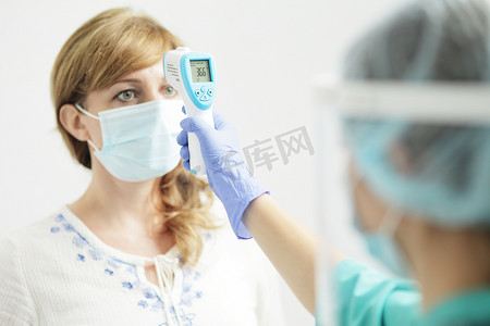新冠防护摄影照片_穿制服的女医务人员用高温计测量妇女的体温