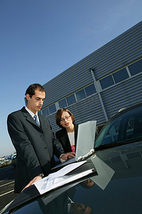 商务夫妇在汽车引擎盖上使用笔记本电脑