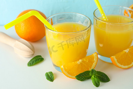 平躺组合物，包括新鲜橙汁、木制榨汁机、薄荷、橙子和木制榨汁机，放在白色桌子上，背景为彩色，特写。