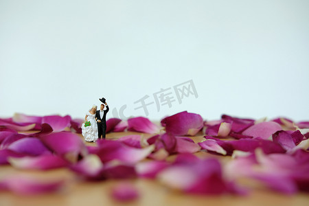 婚礼邀请函摄影照片_微型摄影-户外婚礼/花园婚礼概念，新娘和新郎在红玫瑰花堆上行走