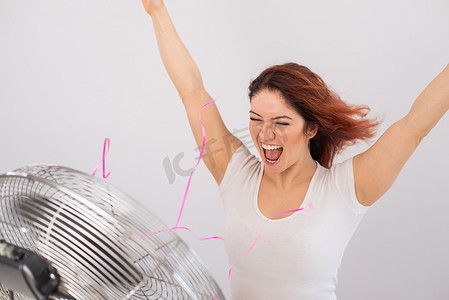 快乐的白种女人享受着白色背景下电风扇吹来的风。