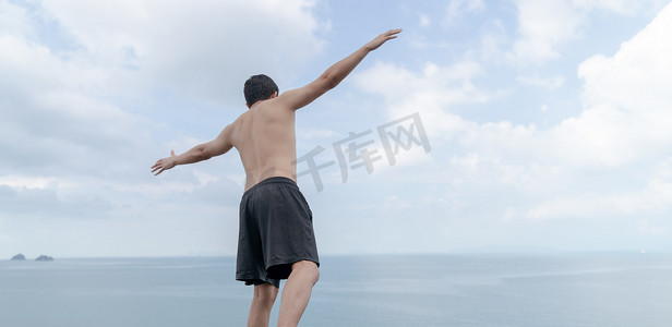 背影张开双手摄影照片_男人的背影在海洋和天空中欣喜地张开双手。