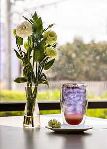 一杯加柠檬水的苏打饮料、橙汁搅拌器蝴蝶豌豆汁 (Anchan) 冷清爽饮料或加冰的饮料 一束白玫瑰放在白色桌子上的玻璃花瓶里。