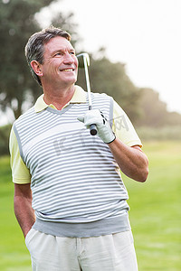 高尔夫球手站着挥动球杆，对着镜头微笑