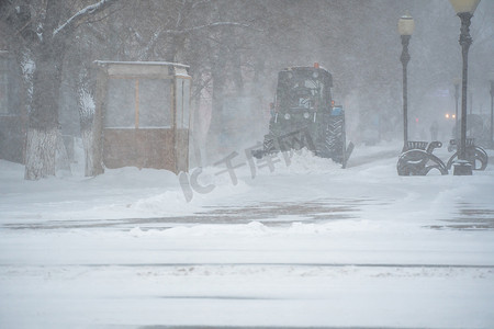 积雪摄影照片_除雪设备、公用事业和市政服务正在清除暴风雪、暴风雪和暴风雪中街道上的积雪。冬天的天气状况。下雪的恶劣天气状况