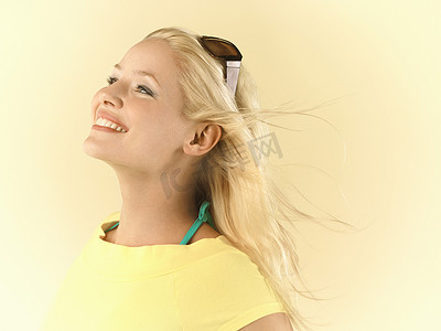 一位年轻女子的特写侧视图，她的金发在黄色背景下随风飘扬