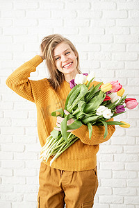 美女拿花摄影照片_穿着黄色衣服的快乐美女拿着一束郁金香