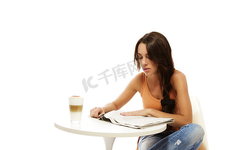 年轻女子在桌边看报纸，喝着拿铁玛奇朵咖啡