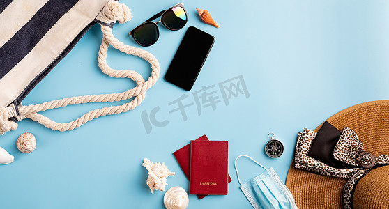 蓝色背景中带夏帽、智能手机、护照、太阳镜和指南针的平躺式旅行物品