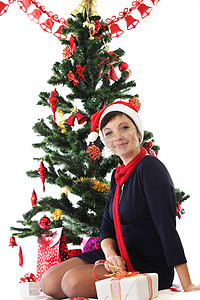 圣诞衣服摄影照片_圣诞树下戴着圣诞帽的微笑女人