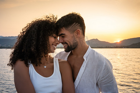 快乐的混血夫妇，留着胡子的白人帅哥和她可爱的西班牙裔女友，面对面微笑着看着对方，夕阳落在湖水上 — 日落时分的多民族恋人