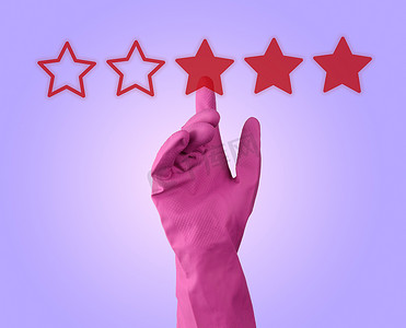 红色的星摄影照片_淡紫色背景中的红色评级星和戴着粉色橡胶手套的手