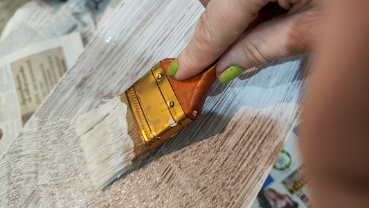 手绘房屋装饰摄影照片_女人手绘在木板上，用刷子装满白色油漆。