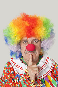 小丑背景摄影照片_浅灰色背景下手指放在下巴上的愤怒高级男性小丑的肖像