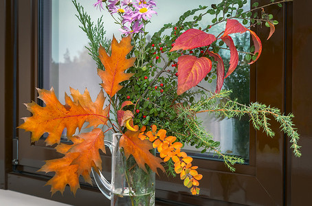 窗户和窗台摄影照片_窗台上有一束秋天的花朵和叶子。
