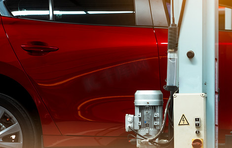 汽车修理厂有选择地关注红色闪亮的汽车和带电机和电机控制箱的升降机杆。