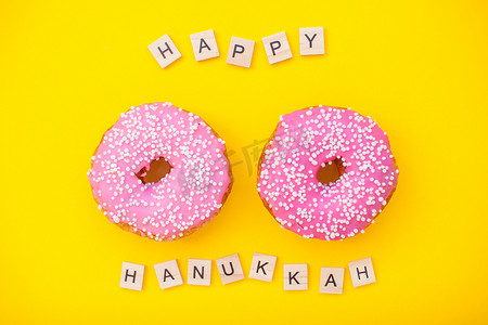 光明冰砖摄影照片_黄色背景中的粉红色美味甜甜圈和木块上的铭文光明节快乐