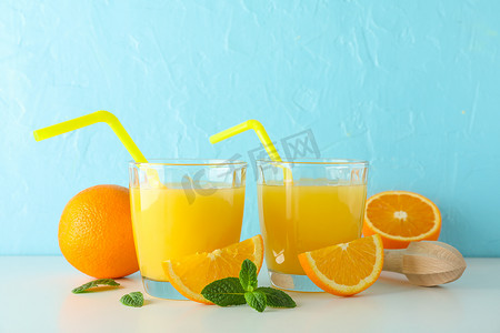平铺组合物，包括新鲜橙汁、木制榨汁机、薄荷、橙子和木制榨汁机，放在白色桌子上，背景为彩色，文字空间。