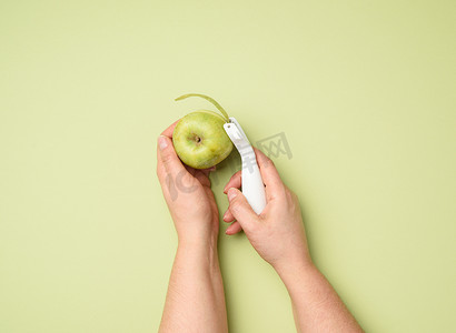 女性手拿着一把塑料刀，用于清洁绿色背景中的蔬菜、水果和青苹果