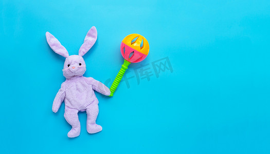 蓝色背景上有彩色婴儿摇铃的兔子玩具。