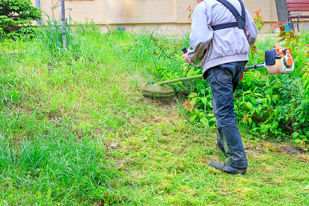 一名工人在城市草坪难以触及的区域用工业汽油修剪机修剪高草。