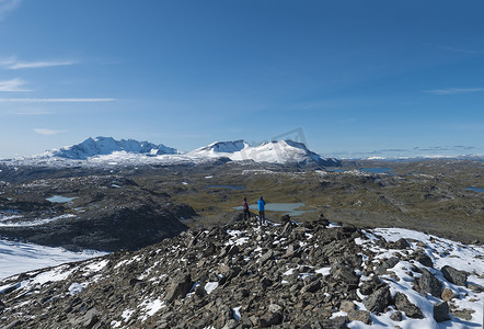 两位徒步旅行者在挪威西部尤通黑门国家公园的雪山和蓝色湖泊上，从 Krossbu 的 Smorstabbreen 冰川脚下欣赏美景