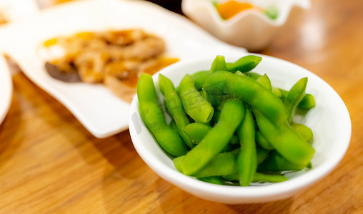 在日本餐厅的木桌上，毛豆或青豆在白碗里漂白。