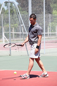 男子站在室外网球场上用球拍弹跳球