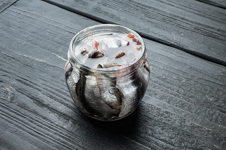 小木桌摄影照片_罐头凤尾鱼，在玻璃瓶中，在黑色木桌背景中